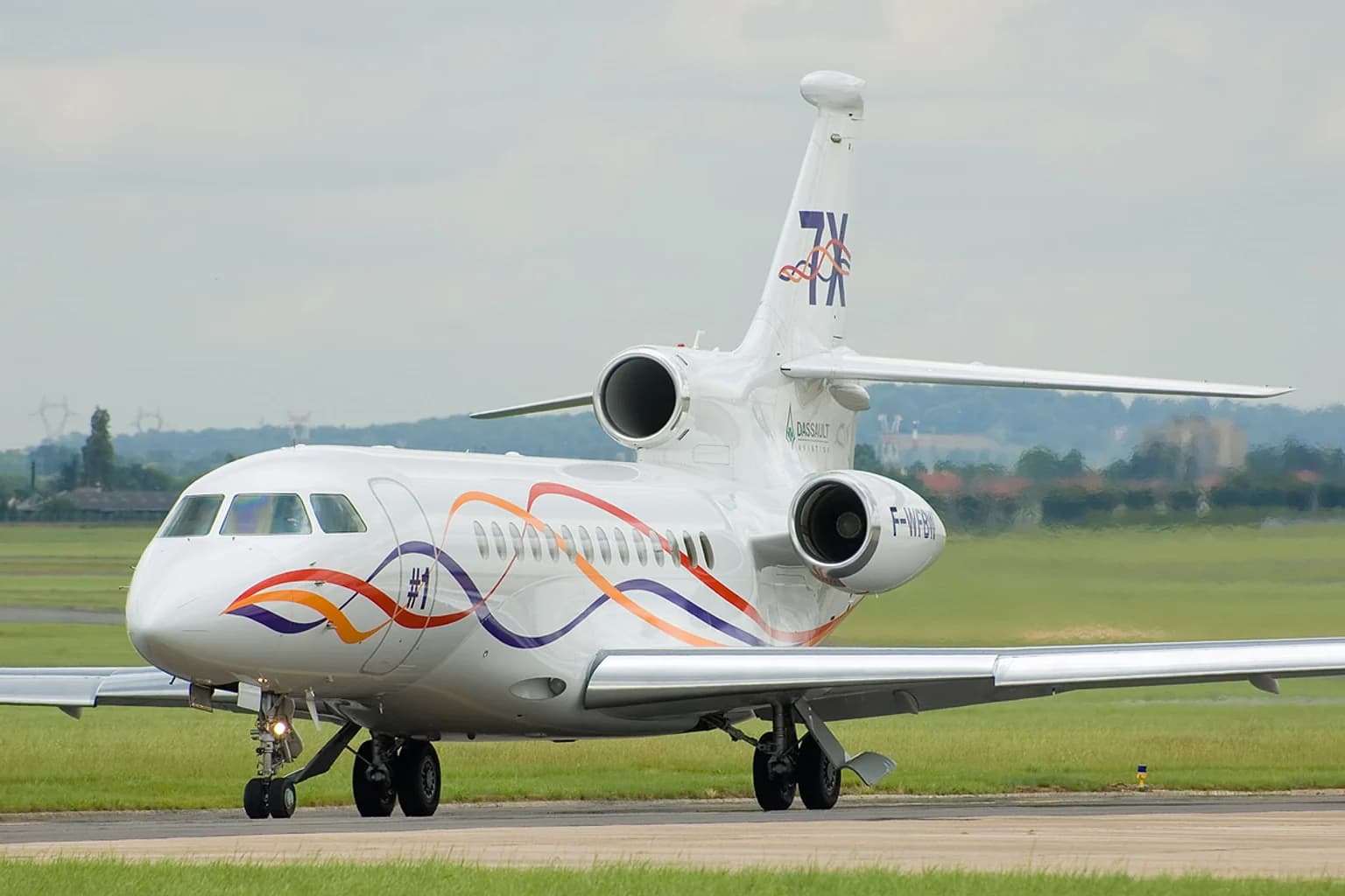 Dassault Falcon 7X business jet on a runway beside green fields.