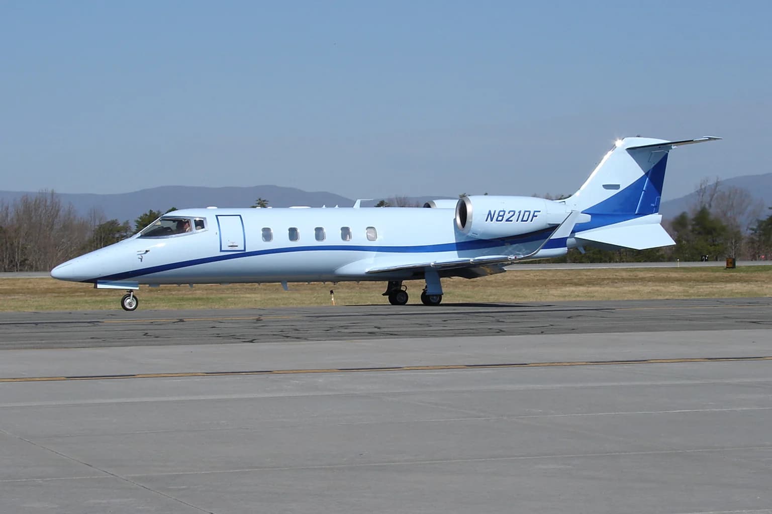 Learjet 60 business jet on an airport apron with mountains behind it.